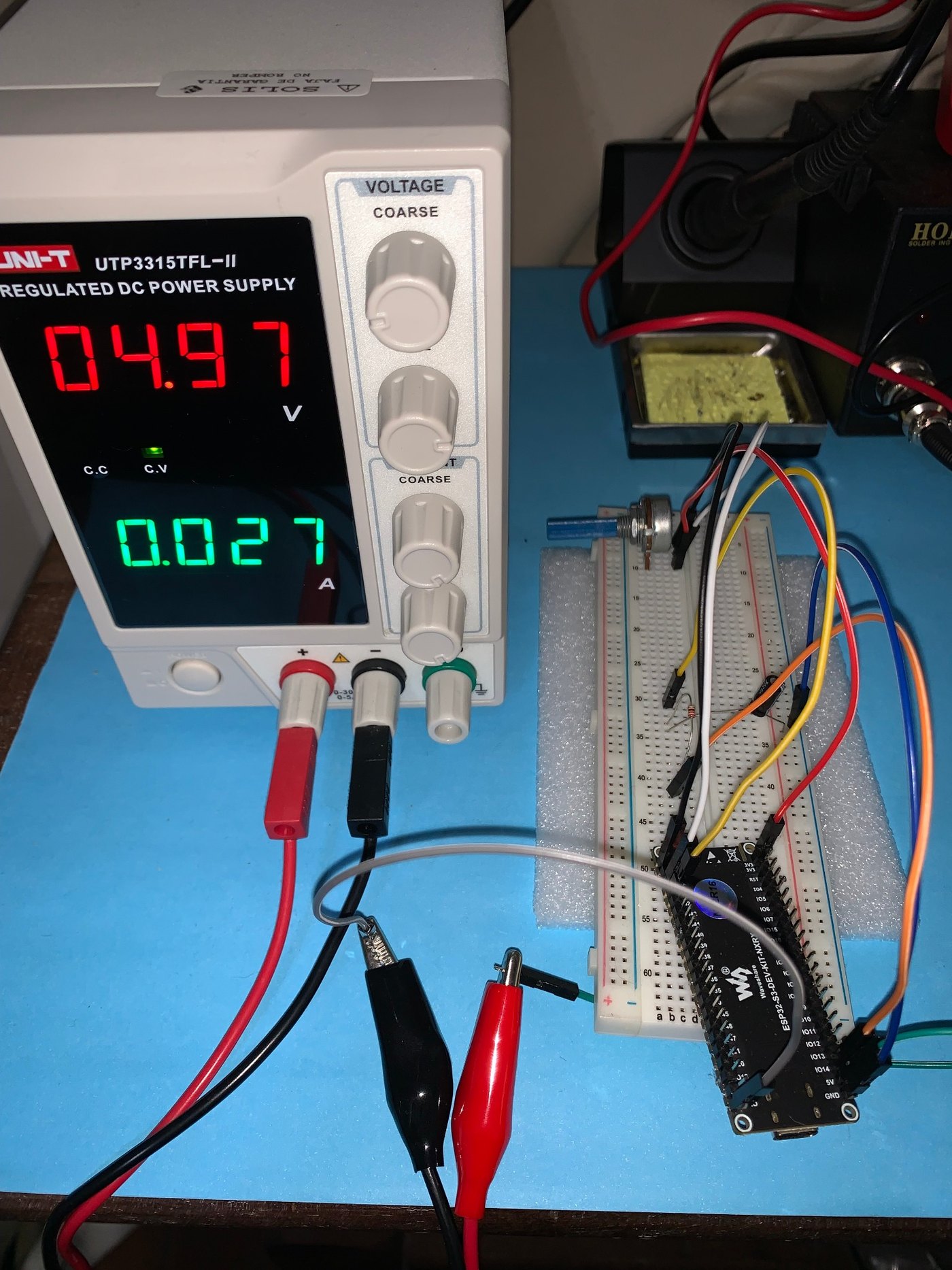 UNI-T regulated bench supply displaying 4.97 volts and 0.027 amps beside the physical ESP32-S3 OSH test setup
